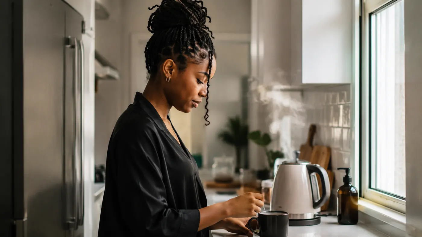Electric kettle steaming on a narrow apartment kitchen counter with a mug and tea bag set out beside it