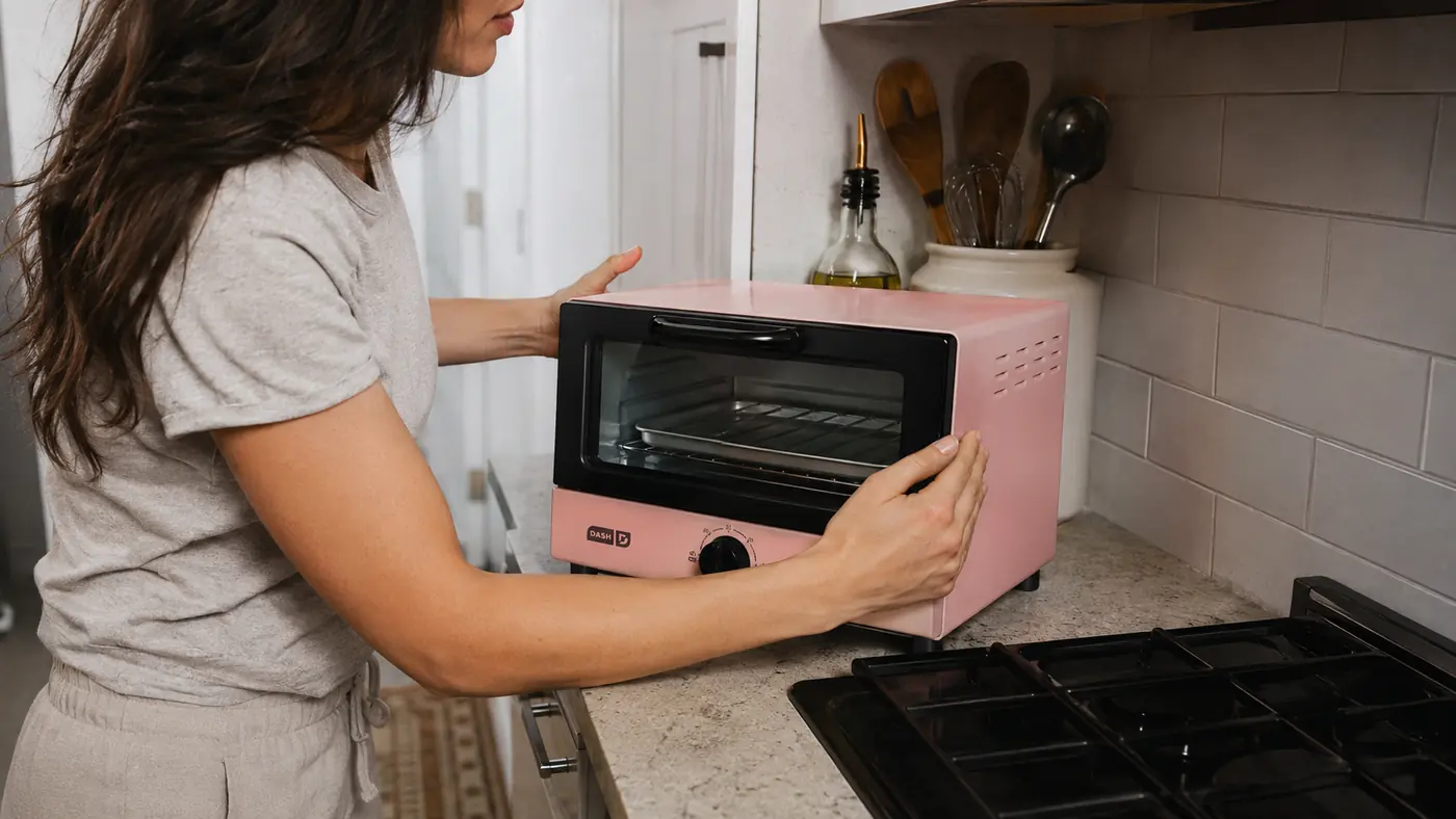 Hand setting the Dash Mini Toaster Oven onto a cleared strip of counter next to the stove