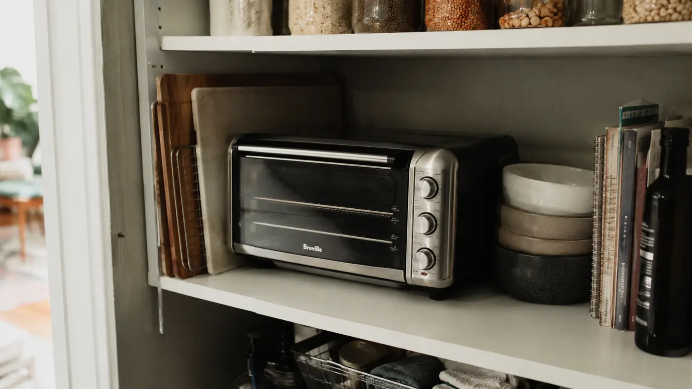 Dash Mini Toaster Oven tucked on a shelf above the counter next to a cutting board when not in use