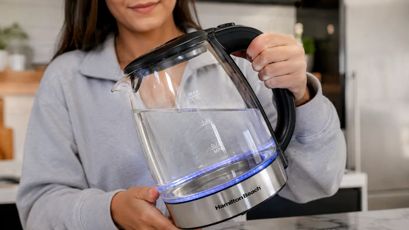 Hand holding the Hamilton Beach kettle at an angle to show the water fill line markings against the actual usable capacity
