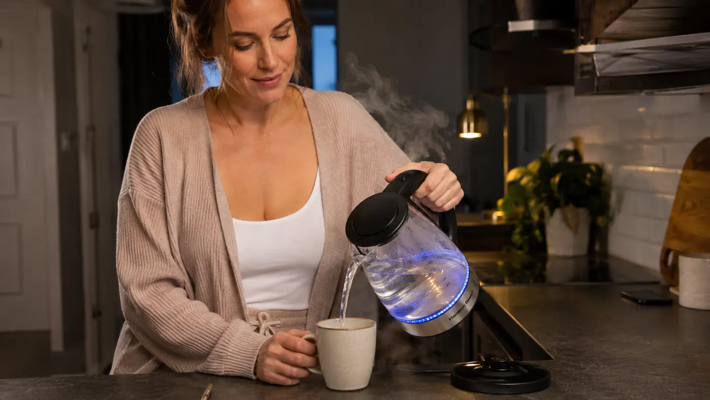 Hand pouring hot water from a small electric kettle into a mug on a narrow apartment counter