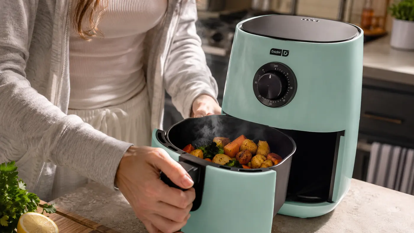 Hand shaking the Dash Air Fryer basket halfway through cooking to check on roasted vegetables