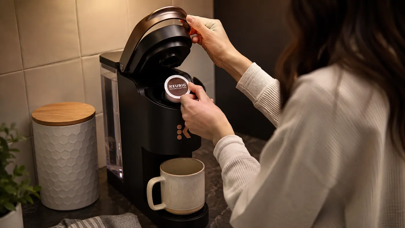 Hand placing a K-Cup pod into the top of the Keurig K-Mini Mate before brewing